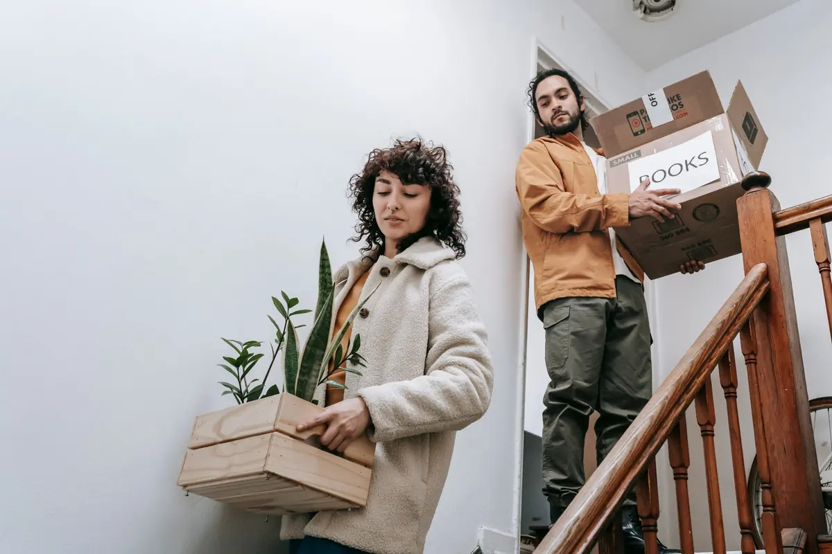 Zwei Personen tragen Bücherkartons über eine Innentreppe